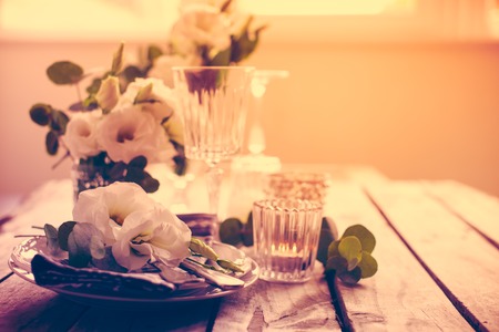 Table setting with white flowers, candles and glasses on old vintage rustic wooden table. Vintage summer wedding table decoration.の写真素材