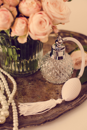 Elegant composition in retro style, vintage perfume bottle and a bouquet of roses on a silver tray on ladies dressing tableの写真素材