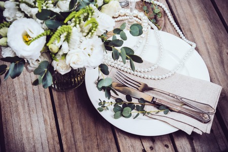 Vintage wedding table decor, tableware and pearl beads, flower bouquet and wine glasses on an old wooden boardの写真素材