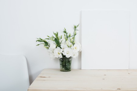 White interior decor, fresh natural flowers in vase and empty canvas on table