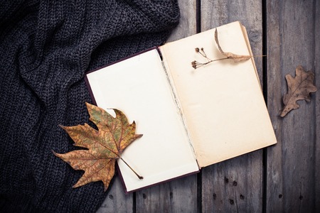 Open empty vintage book and knitted sweater with autumn leaves on old wooden board backgroundの写真素材