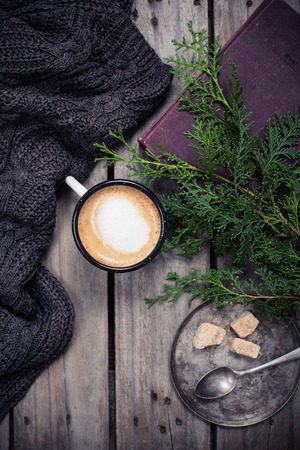 Cozy winter decoration, branch of spruce, warm sweater and a cup of coffee with sugar on old vintage wooden boardの写真素材