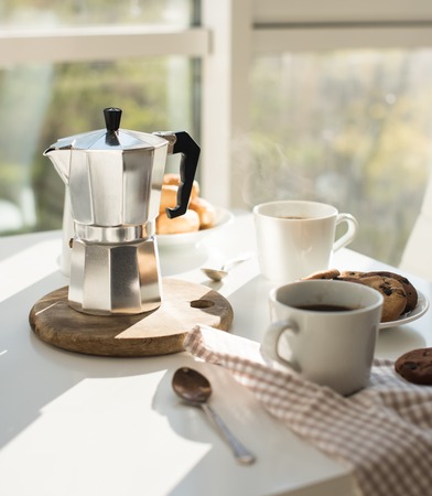 Early morning french home breakfast, coffee and cookies on the table near window in bright sunlight, white interiorの写真素材