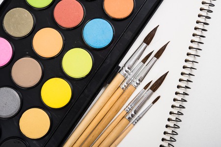 Watercolor paint set and new brushes with clean paper on artist's work desk, creative artistic tools isolated on white background closeupの写真素材