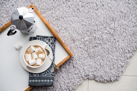 Warm cozy home. Tray and cup of coffee with marshmallows on a floor, comfortable indoorsの写真素材