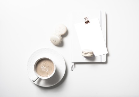 White flat lay with beige macaroons, coffee cup, notepad and posの写真素材