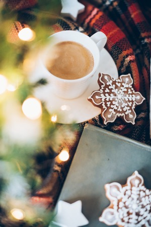 Christmas decoration with a cup of coffee, gingerbread and plaid blanket, new year lights bokeh...