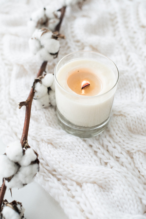 Burning hand-made candle with cotton branch on white cozy winterの写真素材