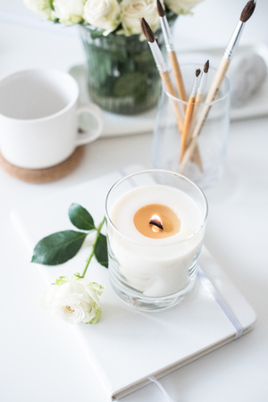 White room interior decor with burning hand-made candle and bouquet rosesの写真素材
