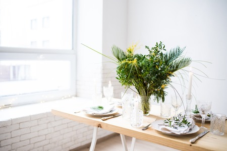 Beautiful springtime table setting with green leaves and mimosa branches, bright white table dinner...