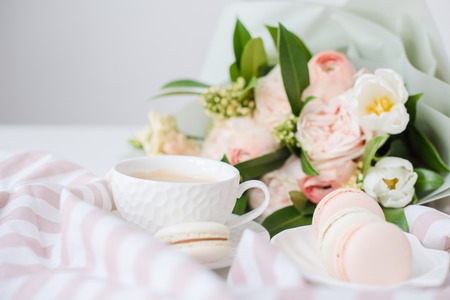 Elegant sweet dessert macarons, cup of coffee and pastel colored beige flowers bouquetの写真素材