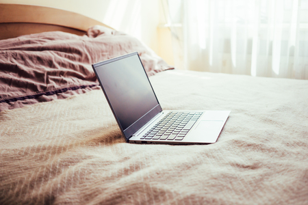 New laptop with blank screen on bed blanket in home bedroom interiorの写真素材