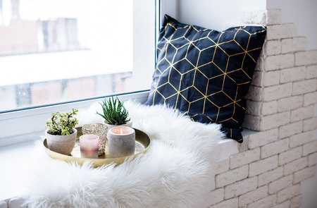 Cozy real home decoration, burning candles on golden tray with pillow on white faux fur on windowsillの写真素材