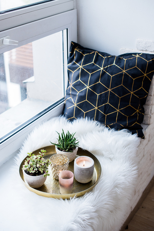 Cozy real home decoration, burning candles on golden tray with pillow on white faux fur on windowsillの写真素材