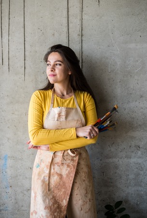 Young beautiful lady artist in apron with paint stains in her loft artistic studioの写真素材