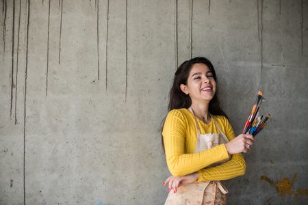 Young beautiful lady artist in apron with paint stains in her loft artistic studioの写真素材