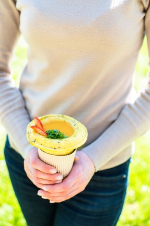 Woman holding healthy vegan street food in her hands, fresh hot vegetable soup in cup