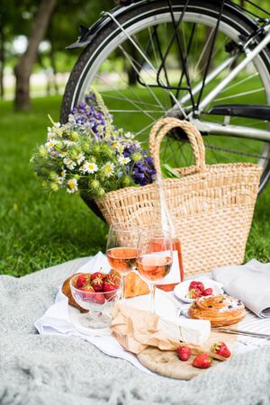 Beautiful summer picnic with strawberries, cheese and rose wine on the lawn in the city parkの写真素材