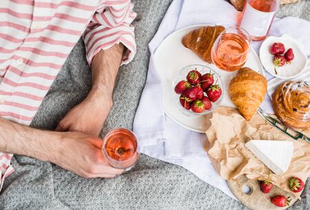 Mans hand holding glass of rose wine, summer picnic with cheese and wineの写真素材