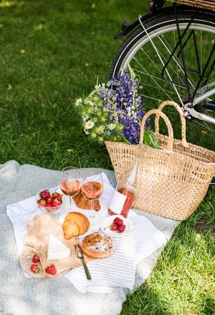 Beautiful summer picnic with strawberries, cheese and rose wine on the lawn in the city parkの写真素材
