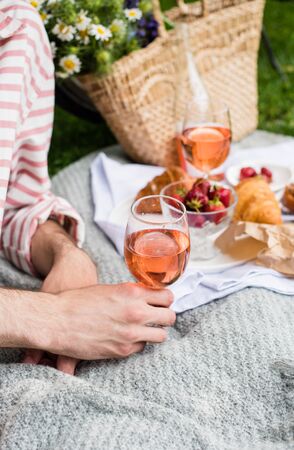 Mans hand holding glass of rose wine, summer picnic with cheese and wineの写真素材