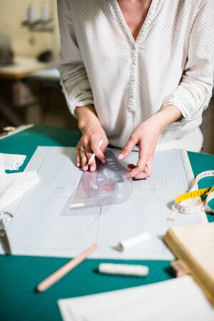 Hands of lady tailor working in her studio, tools and fabric samples on the sewing tableの写真素材