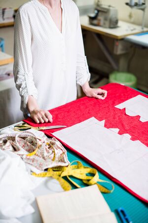 Hands of lady tailor working in her studio, tools and fabric samples on the sewing tableの写真素材