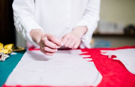 Hands of lady tailor working in her studio, tools and fabric samples on the sewing table