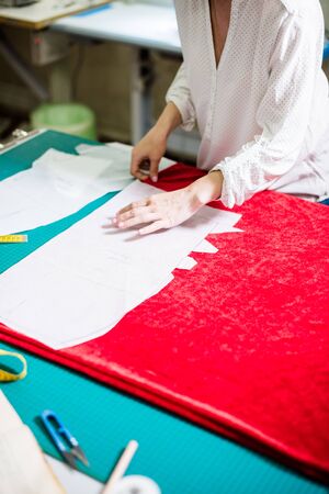Hands of lady tailor working in her studio, tools and fabric samples on the sewing tableの写真素材