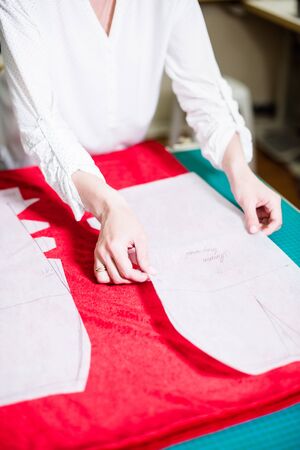 Hands of lady tailor working in her studio, tools and fabric samples on the sewing table