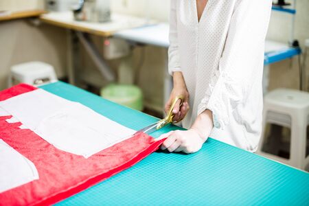 Hands of lady tailor working in her studio, tools and fabric samples on the sewing tableの写真素材
