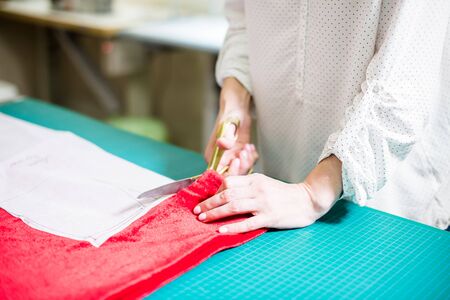 Hands of lady tailor working in her studio, tools and fabric samples on the sewing tableの写真素材
