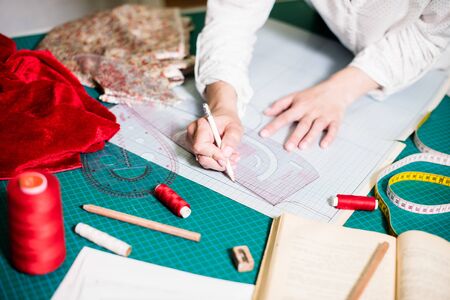 Hands of lady tailor working in her studio, tools and fabric samples on the sewing table