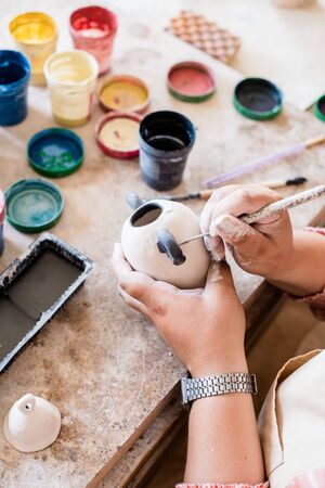 Lady ceramic artist working in her studio interior, womans hands painting objects
