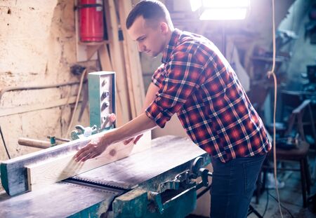 Young handsome joiner working with wood in his carpentry workshopの写真素材