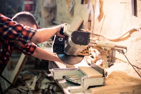 Young handsome joiner working with wood in his carpentry workshop