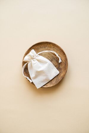 Small linen bag in wooden plate on beige backgroundの写真素材