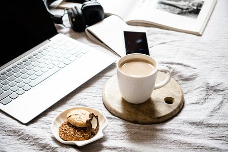 Real home workplace, laptop with cup of coffee with cookies on bed with cozy blanketの写真素材