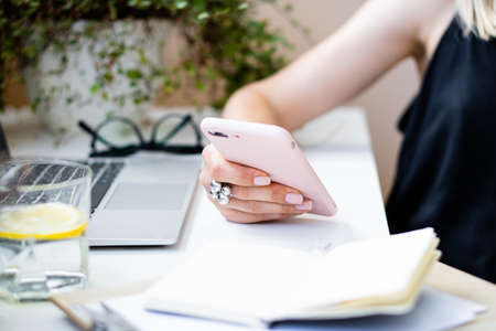 Womans hand holding smartphone in cozy summer office with laptop and green plantsの写真素材
