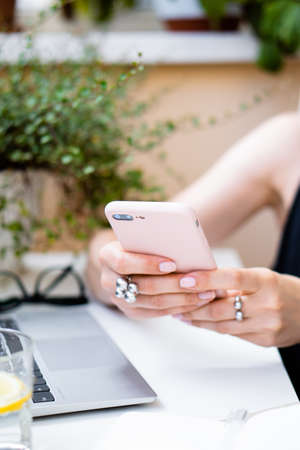 Womans hand holding smartphone in cozy summer office with laptop and green plantsの写真素材