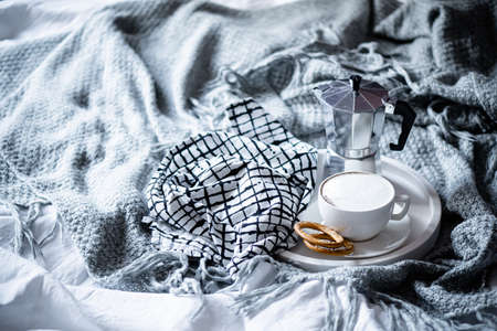Cup of coffee on tray in cozy winter bad with wool blanket