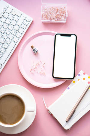 Lady freelancers home pastel pink workplace, cup of coffee and smartphone mock-upの写真素材