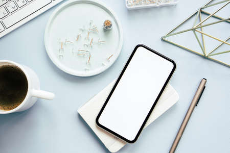 Lady freelancers home pastel blue workplace, cup of coffee and smartphone mock-up on tabletopの写真素材