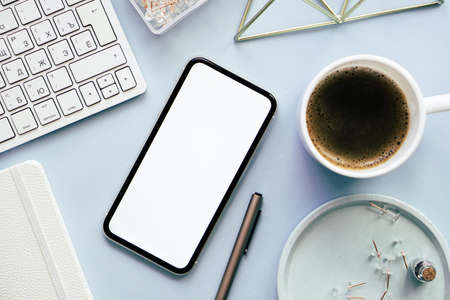 Lady freelancers home pastel blue workplace, cup of coffee and smartphone mock-up on tabletopの写真素材