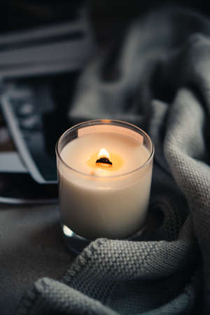 Burning candle in glass with wooden wick, handmade natural wax candle with knitted blanketの写真素材