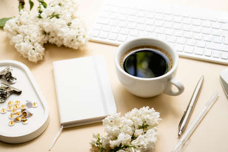 Beige and white work space with coffee cup, notepad and lilac flowersの写真素材