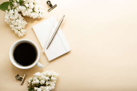 Beige and white work space with coffee cup, notepad and lilac flowersの写真素材