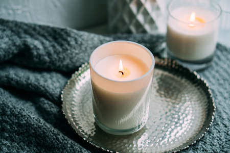 White burning candle in glass candleholder on vintage metal tray, warm cozy homeの写真素材
