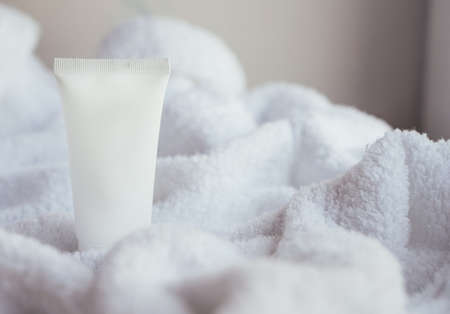 Clean white cosmetic cream tube on fluffy white cotton towel background, mock-up and design readyの写真素材