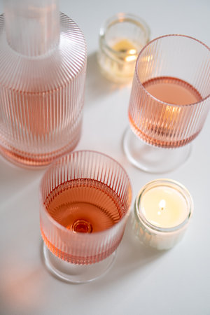 Rose wine in trendy ribbed wineglasses and decanter on white tableの写真素材